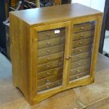 A polished beech table-top collector's chest, the 2 glass panelled doors revealing 18 short fitted