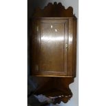 A Georgian oak hanging corner cupboard, with panelled door and shelf under, L140cm