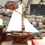 A large wooden-hulled model pond yacht, with wire and string rigging, modern sails and fitted stand,