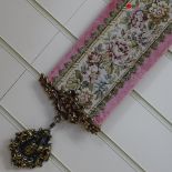 A machine embroidered tapestry panel curtain tieback with cast-brass mounts, overall length 133cm