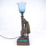A patinated spelter table lamp in the form of a woman at a fountain, with blue glass shade,