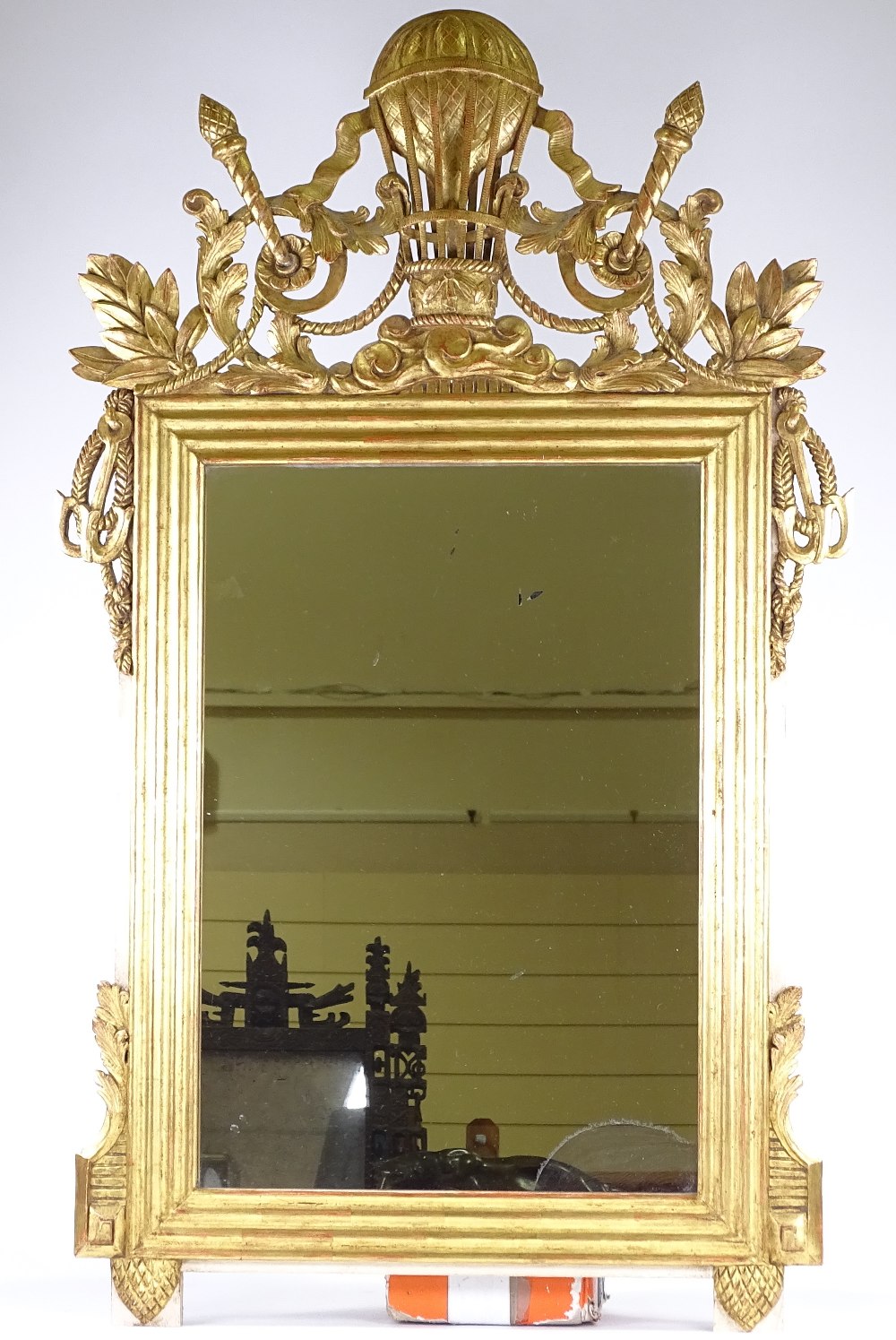 An ornate carved and gilded wood-framed wall mirror in Louis XVI style, with carved and pierced