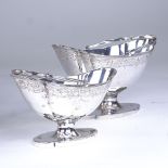 A graduated pair of George III silver boat-shaped pedestal sugar baskets, reeded swing handles