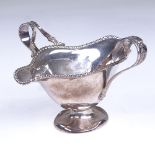 An Edwardian silver 2-handled double-spouted pedestal sauce boat, gadrooned rim with relief floral