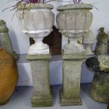 A pair of weathered concrete garden urns, on pedestal stands, overall height 135cm