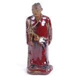 An 18th century pottery figure of a man with sang de boeuf glaze robes, height 18cm Tiny chip on the