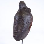 A small African carved wood mask, height 25cm, on modern stand