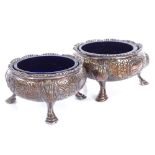 A pair of Victorian silver salt cellars, relief embossed floral decoration on 3 shell feet, with