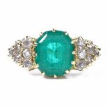 An early 20th century unmarked gold solitaire emerald ring, diamond cluster shoulders, total diamond