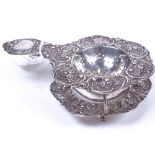 A German silver tea strainer and matching base, with allover relief embossed floral and foliate