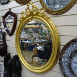 A large early 20th century giltwood oval bevel-edge wall mirror, with ribbon pediment, overall