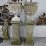 A pair of weathered concrete garden urns, on pedestal stands, overall height 135cm