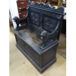 An early 20th century carved and panelled oak settle, with lion supports and rising seat, W90cm,