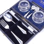 A pair of glass salts with silver collars and spoons, and a cased spoon and fork set