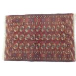 Turkman Bokhara woollen rug, having three rows of guls against a deep red ground, size approx.