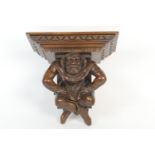 German carved walnut figural clock bracket, the plinth supported by a crouching peasant in