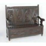 Carved oak box settle, circa 1900-1920, having a four foliate carved panel back and scroll arms,