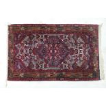 Iranian woollen rug, central lozenge reserve against a fawn and deep red field with a geometric