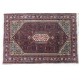 Iranian woollen rug, having a central fawn reserve against a lozenge shaped deep red ground,