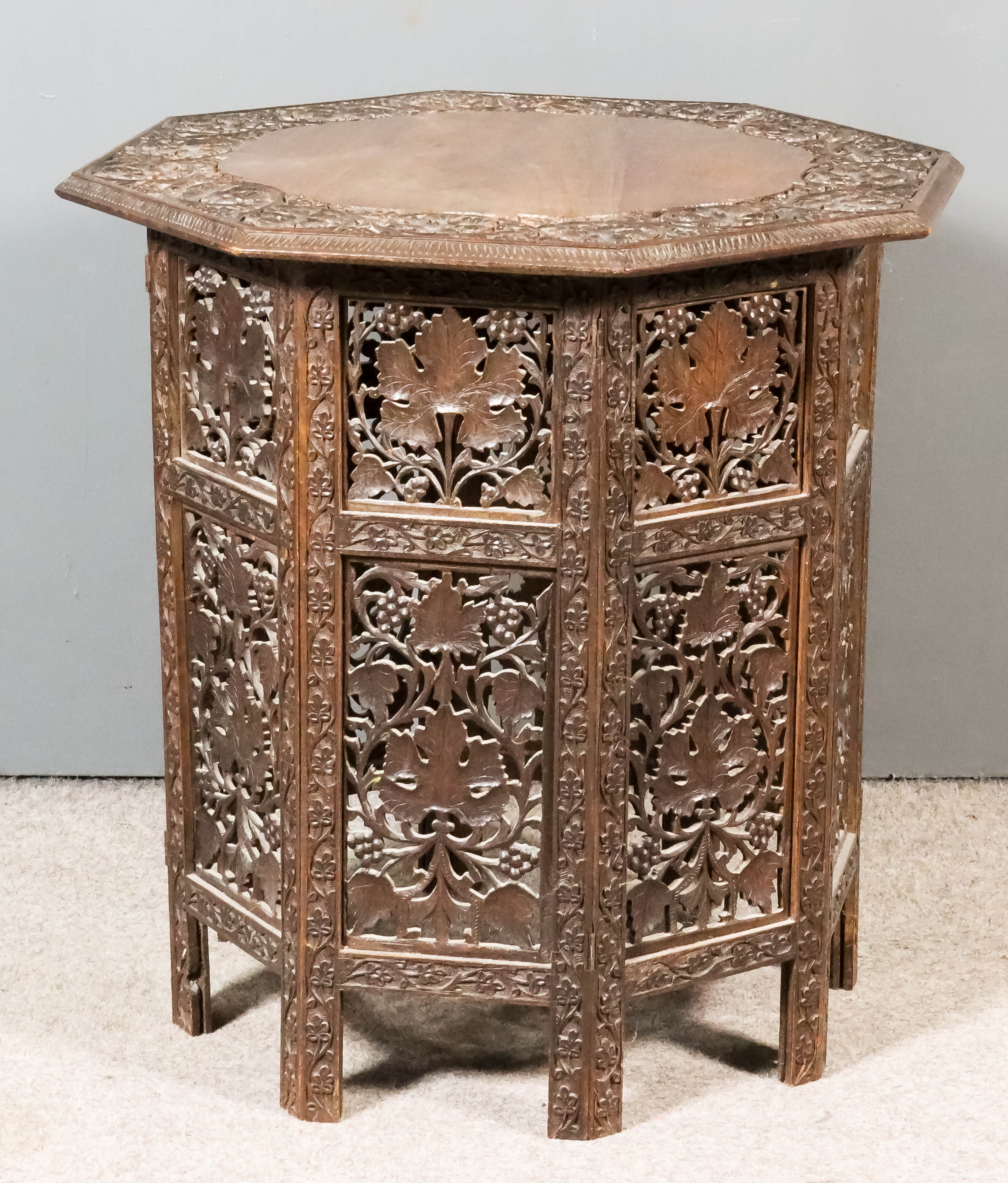 A Near Eastern Carved Wood Octagonal Occasional Table, the top carved with a band of fruiting vines,