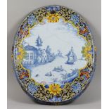 A Dutch Delft Oval Wall Plaque, 19th Century, painted in blue with a river scene, the border