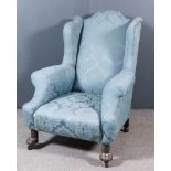 An Early 20th Century Wingback Easy Chair, with outscrolled arms, upholstered in blue cloth, on