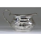 A Chinese Silvery Metal Oval Cream Jug, the bulbous body chased and embossed with four panels of