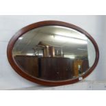 AN OVAL BEVELLED EDGE WALL MIRROR IN MAHOGANY FRAME WITH FEATHERED LINE INLAY