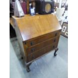 A WALNUTWOOD BUREAU WITH SLOPING FALL FRONT AND THREE GRADUATED LONG DRAWERS BELOW, ON CABRIOLE