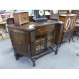 1920's CARVED OAK INVERSED BREAKFRONT SIDE CABINET WITH CENTRE DOOR OVER THE GLAZED DOORS, THE