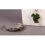 SILVER TORQUE BANGLE pierced with scrolls, the top set with an oval garnet and a carved green