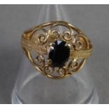 9ct GOLD DRESS RING, the broad circular scrolled wire pattern top set with a dark oval sapphire,