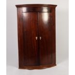 GEORGE III FIGURED MAHOGANY BOW FRONTED CORNER CUPBOARD, of typical form with flame cut frieze,