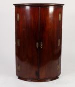 EARLY NINETEENTH CENTURY MAHOGANY BOW FRONTED CORNER CUPBOARD, of typical form with six exposed