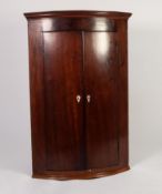 GEORGE III FIGURED MAHOGANY BOW FRONTED CORNER CUPBOARD, of typical form with flame cut frieze,