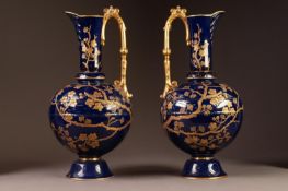 PAIR OF LATE NINETEENTH CENTURY OLD HALL POTTERY EWERS, each of footed form with moulded gilt handle