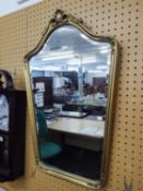 A BEVELLED EDGE WALL MIRROR, CARTOUCHE SHAPED, IN EMBOSSED GILT FRAME