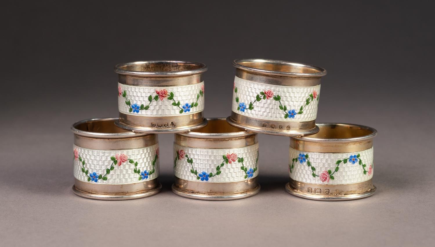 GEORGE V SET OF FIVE SILVER AND GUILLOCHE ENAMELLED NAPKIN RINGS, each painted with floral swags