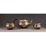 INTER-WAR YEARS THREE PIECE SILVER TEA SERVICE of oval panelled form, the teapot with black wood