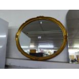 AN OVAL WALL MIRROR IN SWEPT GILT FRAME