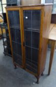 AN OAK TWO DOOR NARROW BOOKCASE, WITH LEAD GLAZED DOORS