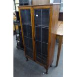 AN OAK TWO DOOR NARROW BOOKCASE, WITH LEAD GLAZED DOORS