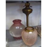 A TALL BRASS OIL TABLE LAMP WITH SMALL PINK GLASS SHADE AND GLASS FUNNEL AND ANOTHER PINK AND