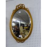A SMALL OVAL BEVELLED EDGE WALL MIRROR IN GILT FRAME WITH RIBBON PEDIMENT