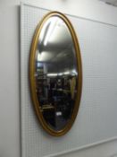 A NARROW OVAL BEVELLED EDGE WALL MIRROR, IN GILT FRAME