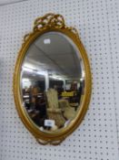 A SMALL OVAL BEVELLED EDGE WALL MIRROR IN GILT FRAME WITH RIBBON PEDIMENT (51cm high)