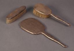 GEORGE V THREE PIECE LADY?S ENGINE TURNED SILVER CLAD DRESSING TABLE HAND MIRROR AND BRUSH SET,