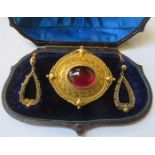 CASED UNHALLMARKED YELLOW METAL VICTORIAN MOURNING BROOCH SET WITH CENTRAL RUBY COLOURED STONE.