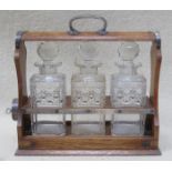 OAK CASED THREE DECANTER TANTALUS WITH SILVER COLOURED CARRY HANDLE (ONE A/F)