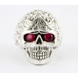 A sterling silver skull shaped ring with ruby set eyes, (Q).